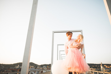 Fashion lovely beautiful couple posing on roof with city background. Young man and sensual blonde outdoor. Lifestyle.