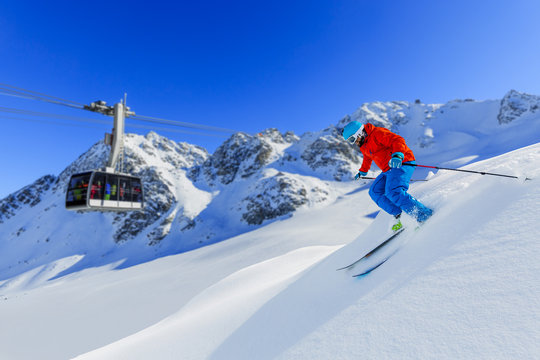 Skier skiing downhill in high mountains in fresh powder snow. Snow mountain range and cable railway in background. Mt Fort Peak Alps region Switzerland.