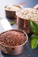 Stack of three Mixed raw quinoa, South American grain, in copper measuring cups with bay laurel leaves on blue background. Healthy and gluten free food.