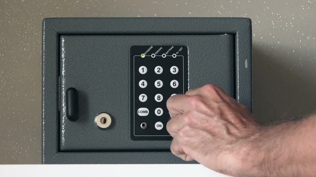 Man opening safety deposit box in hotel, hand typing security code and unlocking the door or the safe.