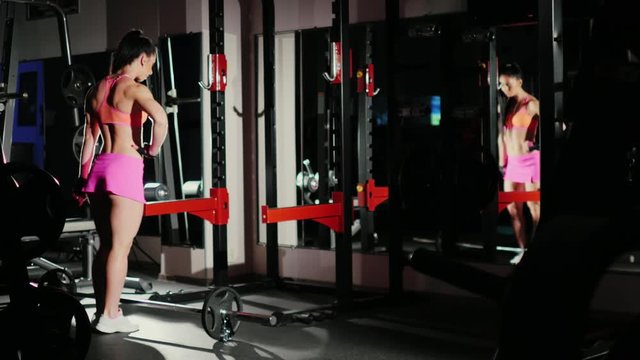 Athletic woman, a professional bodybuilder posing in front of a mirror, shows muscles