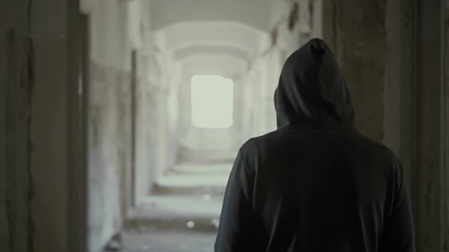 Hooded young man inside destroyed abandoned building,slow motion,dramatic