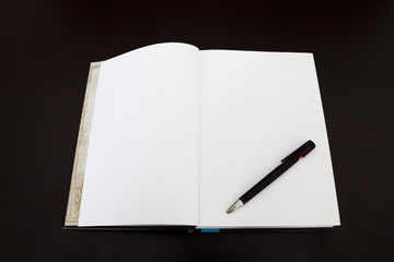 Open book with pen on dark wood desk.