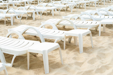 Empty White Plastic Deck Chairs On Sandy Beach.