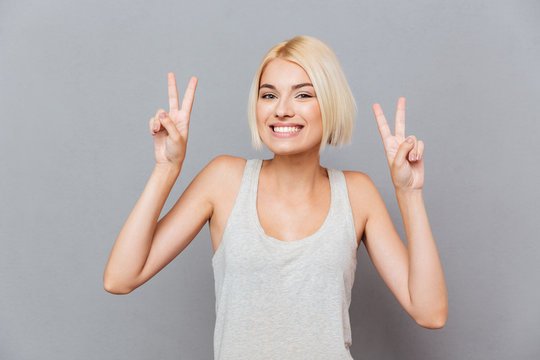Cheerful cute young woman showing peace sign with both hands