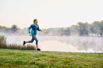 Fit woman running at autumn morning in park