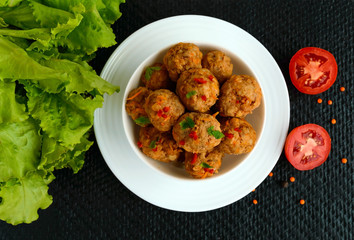 Meat balls with chilli and herbs in a white bowl on a black background. The top view.