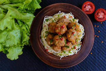 Pasta (spaghetti) with meat balls in a clay bowl on a dark background. The top view.