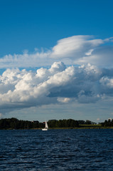Widok na jezioro w po którym płynie jacht żaglowy. Na niebie widać rozbudowujące się chmury Cumulus.