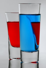Two blue and red cocktail in full glass with own reflections