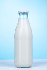 Flasche Milch vor hellblauem Hintergrund.