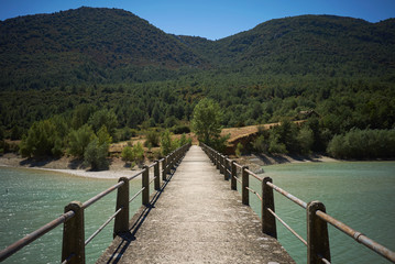 Naklejka premium Walking on a concrete pedestrian bridge over a shallow light blue bay towards wooded hills