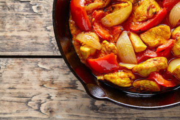Traditional jalfrezi chicken Indian culture spicy meat and vegetables food dish in cast iron pan on vintage wooden table background. Top view