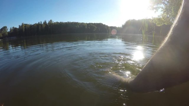Man relaxes by the lake or pond sitting on the edge of a wooden jetty, swing one's feet in the water. Male legs splashing water in the pond. A person's feet relaxing and dangling in a river. Close-up