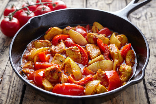 Traditional jalfrezi chicken Indian spicy meat and vegetables dish in cast iron pan on vintage wooden table background