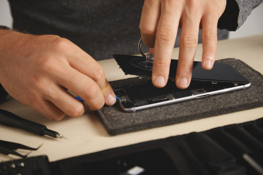 Man uses vacuum plug and plastic opener to remove screen from broken phone, his toolkit with special tools near, close view
