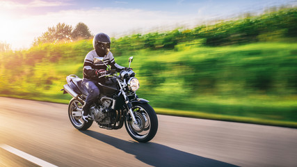 Naklejka premium Mężczyzna jadący na motocyklu, na obrazie duży ruch prędkości, w tle zachód słońca