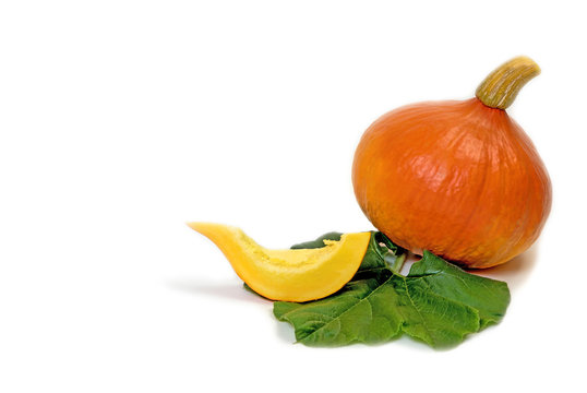 Orange pumpkin, piece of pumpkin and green leaf of the plant are lying on the white background. 