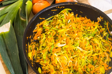 Fried leek and carrot in the pan on the wooden board