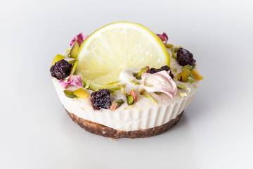 Raw vegan cake with lime and banana, decorated with a slice of lemon, dried cherries and rose petals, close up. 