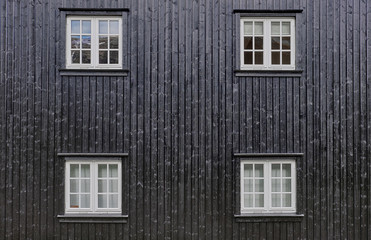 Fototapeta na wymiar Four square white casement windows with mullions, placed symmetrically in a black painted facade with boards fitted as tongue and groove