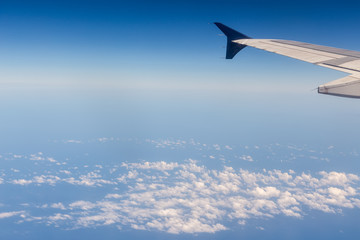 Wing of airplane flying above the clouds in the sky