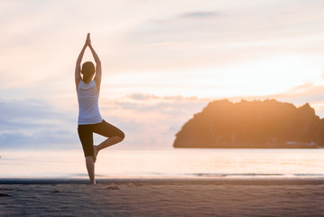 Young woman practicing yoga on the beach at sunset.