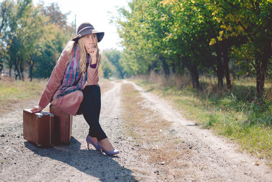 Woman alone with vintage suitcase hitchhiking on empty road outdoors