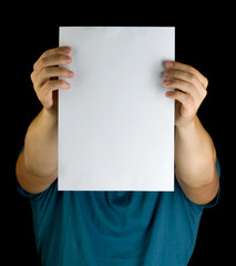 young man holding white blank paper vertically on extended arms copy space advertisement in front of his face isolated black