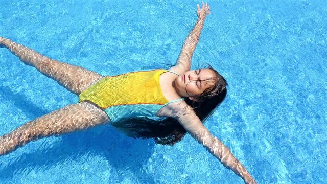 Little girl in swimsuit lying on the water in pool