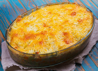 Potato, cheese, meat, carrot, onion and green peas casserole on blue wooden background