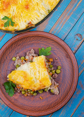 Potato, cheese, meat, carrot, onion and green peas casserole on blue wooden background. View from above, top studio shot