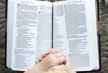 Child's Hands Praying Over Open Holy Bible