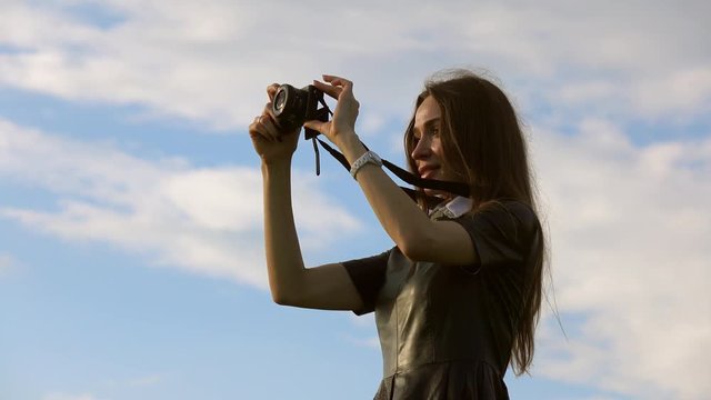 Beautiful brunette girl in black dress against sky taking photos with her compact camera. 4K video