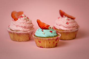 Toned photo of three decorated cupcakes over pink background