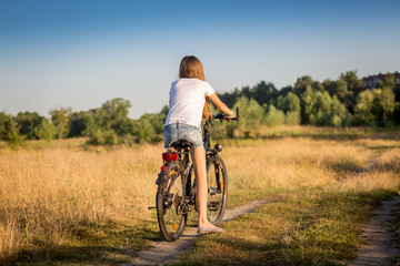 Obraz premium Girl in shorts and t-shirt cycling in meadow at sunset