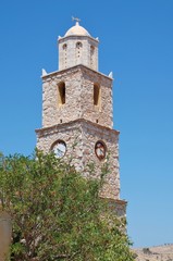 Fototapeta na wymiar The old stone clock tower at Emborio on the Greek island of Halki. The clock has been stopped at four twenty for many years.