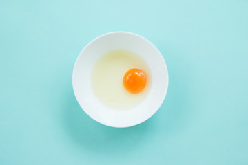 Top view of raw egg in white bowl on blue background.