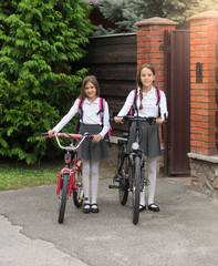 Obraz premium Smiling girls in school uniform with bicycles in front of house