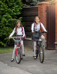 Smiling girls in uniform riding to school on bicycles