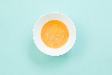 Beat egg in white bolw on blue background.
