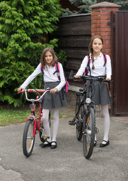 Two smiling girls in school uniform walking with bicycles on str