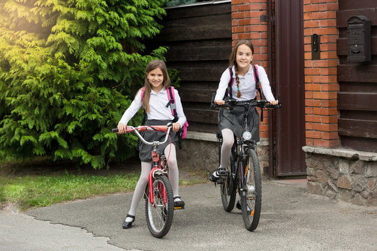 Two girls in school uniform with bags riding to school on bicycl