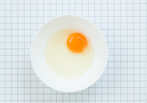 Top view of raw egg in white bowl on pattern  background.
