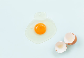 Top view of raw egg with eggshell on soft blue background.