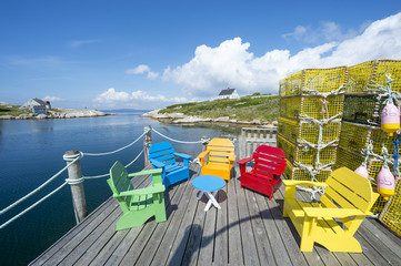 Brightly colored Adirondack chairs sit next to stacks of lobster traps on a deck on the shore of a...