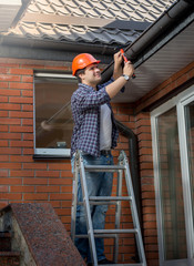 Worker standing on step ladder and repairing gutter on house