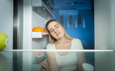 Fototapeta na wymiar Tired woman in pajamas looking inside of refrigerator at late ni