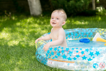 Fototapeta na wymiar Smiling cute baby boy having fun in swimming pool at garden