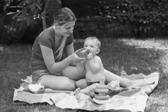 Black and white image of mother feeding her baby at park